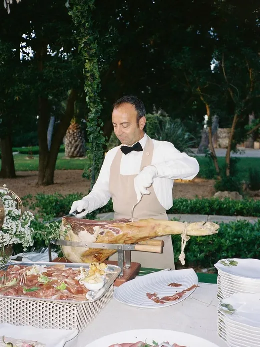 A chef in a white jacket carving ham at an outdoor station