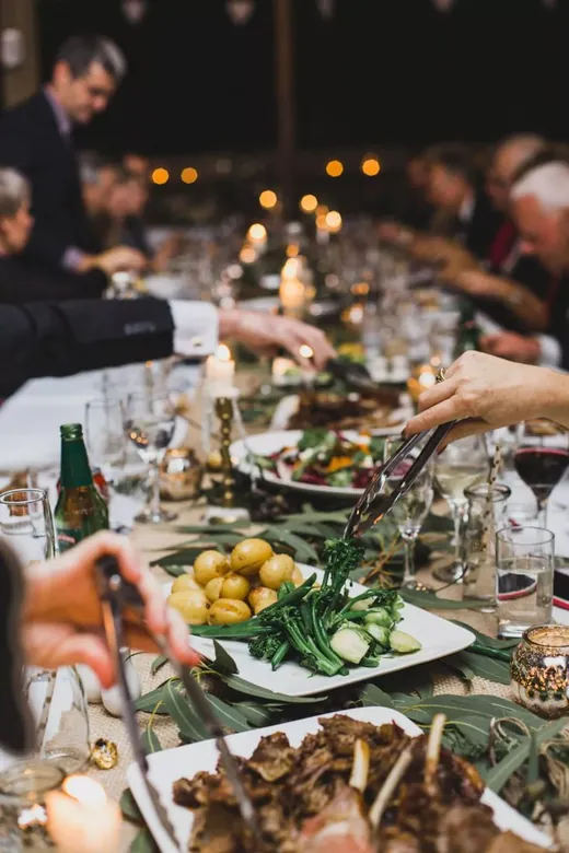 Guests reaching across a long candlelit table laden with sharing dishes